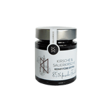 DELIGREECE Kirsche & Sauerkirsche Konfitüre Extra mit 85 % frischen Früchten im Glas – weißes Etikett, silberner Deckel, feine Kirsch-Illustration.