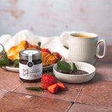 Erdbeer-Konfitüre von DELIGREECE mit frischen Erdbeeren, Croissants, Minze und einer Tasse Kaffee stilvoll angerichtet