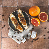 Grapefruit-Marmelade von DELIGREECE mit frisch bestrichenen Brotscheiben und aufgeschnittener Grapefruit dekorativ angerichtet.
