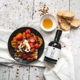 Honig-Balsamico Flasche neben geröstetem Brot, Honigschale und Tomaten-Bruschetta
