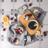 Sauerkirsch-Konfitüre von DELIGREECE mit Joghurt, Kirschen und Zitronenscheiben auf Holzbrett und Stofftuch angerichtet.