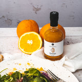 Orangen-Balsamico Flasche neben frischen Orangen und Salatteller