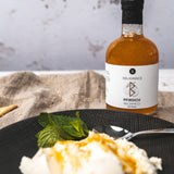 Pfirsich-Balsamico Flasche neben Dessert mit Minze und Löffel