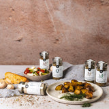 DELIGREECE Gewürzmischungen arrangiert mit griechischem Salat, gerösteten Kartoffeln, Brot und Knoblauch auf rustikalem Untergrund.