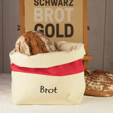 Laib Brot in einer Stoff-Brottasche, im Hintergrund ein Schild ‚SCHWARZ BROT GOLD‘