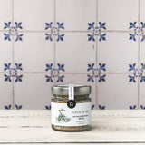 Glas Fleur de Sel mit Wildkräutern (Kreta) auf weißem Holztisch vor blau-weiß gefliester Wand