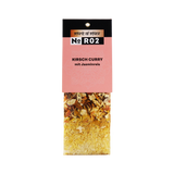 Hängeetikett einer Trockenmischung: Spirit of Spice No R02 – Kirsch Curry mit Jasminreis; unten im transparenten Beutel gelber Jasminreis mit getrockneten Zutaten und Gewürzstückchen.